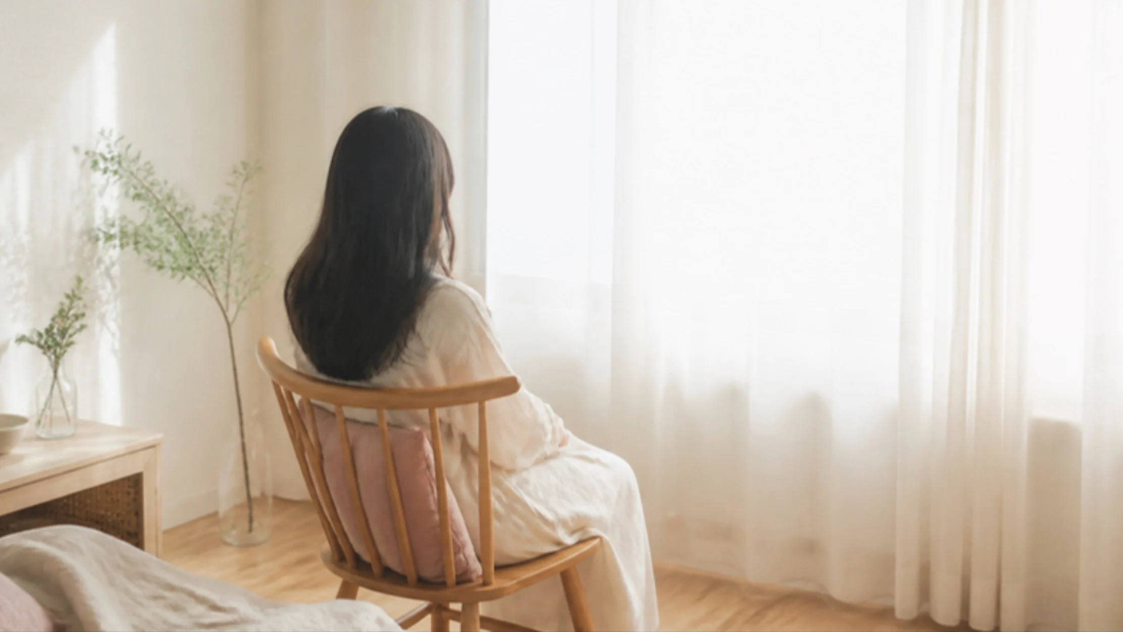 やわらかな光の入る窓辺で、椅子に座って外を眺める人の後ろ姿